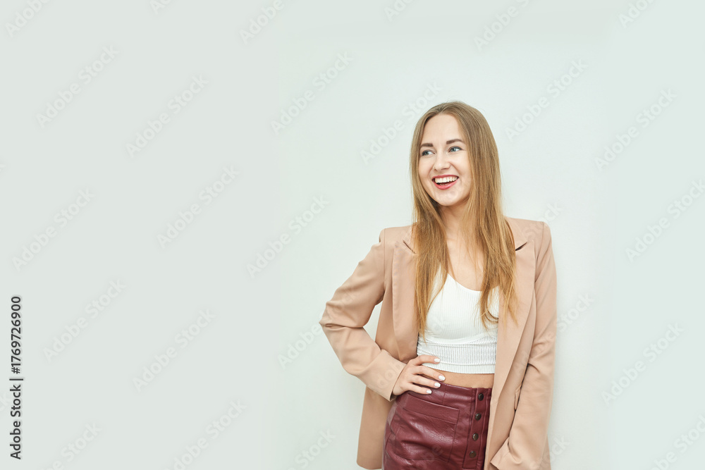 Obraz premium Smiling young caucasian female in beige blazer and red skirt against light background.