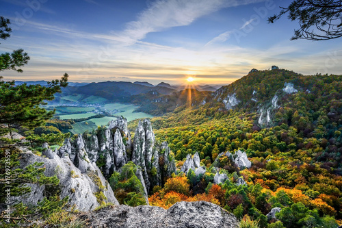 Sunset during the autumn season in the wild Carpathians. Colorful leaves of trees in contrast with white rocks. Blue sky with sun rays of the setting sun.