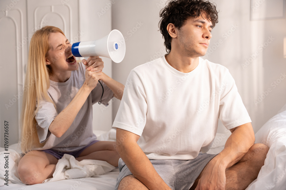 Fototapeta premium Couple arguing in bedroom. woman screaming at her boyfriend. Man ignores screaming woman indoors at home. Young woman arguing with her boyfriend sitting on bed. couple, arguing, yelling, screaming