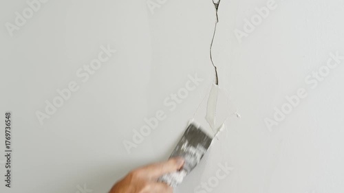A plasterer's hand repairs a wall by applying putty with a spatula, concept of timely repair and maintenance of houses and apartments