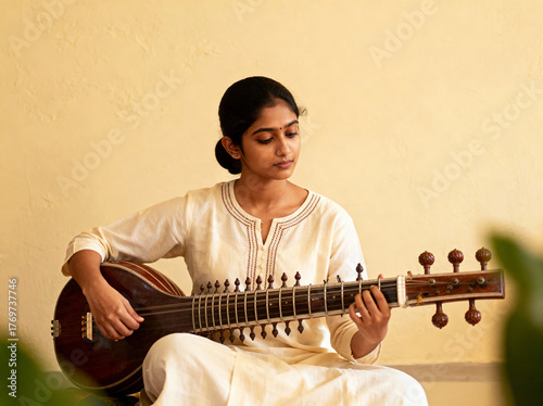 Young Indian woman playing sitar with focused expression, traditional instrument performance in natural light, cultural art