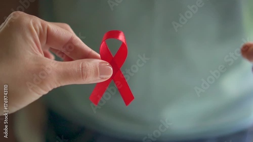 Close-up of male hand offering red awareness ribbon to female hand representing collective support for World AIDS Day awareness.