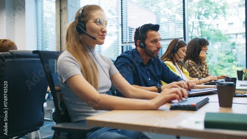 Side view of customer support team working in call center. Focused operators wearing headsets typing on keyboards. Employees providing assistance and communication services in modern office.
