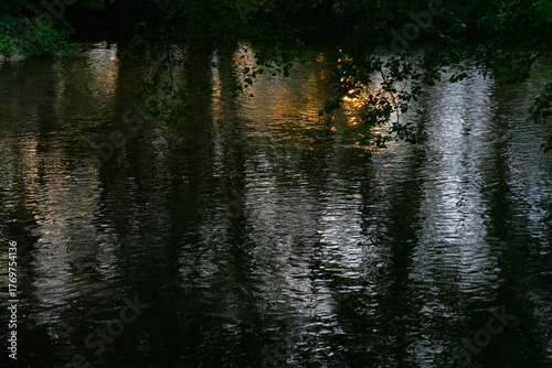 Mysterious atmosphere: reflection of trees and orange sunset in dark water