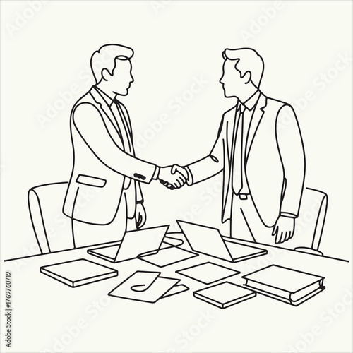 Two businessmen shaking hands over a table with laptops and documents outline