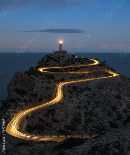 Obraz na plátně Winding coastal road with light trails leading to a lighthouse at dusk