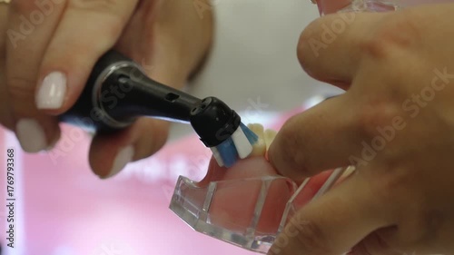 Valmiera, Latvia - October 06, 2025: Dental hygienist demonstrates teeth cleaning technique using electric toothbrush on dental model, camera zooms in