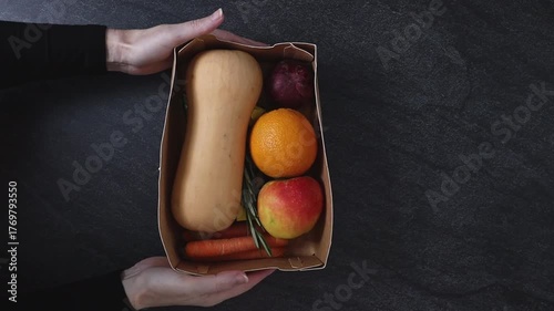 The girl takes the box with the pumpkin soup set from the black stone table.