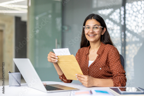 Quadro su tela Young indian woman smiling with excitement as she opens a letter at her desk in