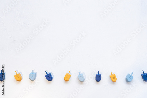 textured border background with blue and yellow wooden dreidels, which are spinning tops played in a game during the Jewish holiday of Hanukkah.