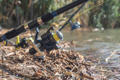 Several fishing rods are arranged in a row. The emphasis is on one of the fishing rods which is in the foreground.
