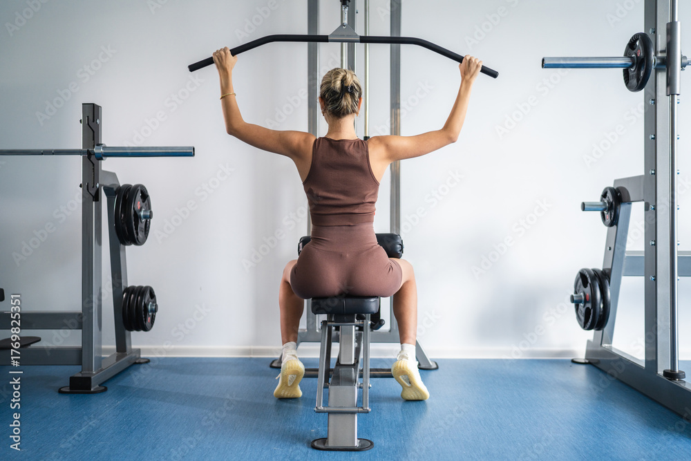 Fototapeta premium Woman performing lat pull down exercise at modern gym