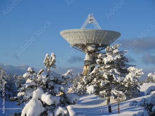 Radio telescope antenna in snowy winter landscape under clear blue sky