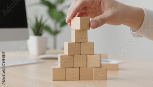 Hand stacking wooden blocks into a pyramid shape, symbolizing business growth, strategic planning, project development, career progression, and hierarchy establishment