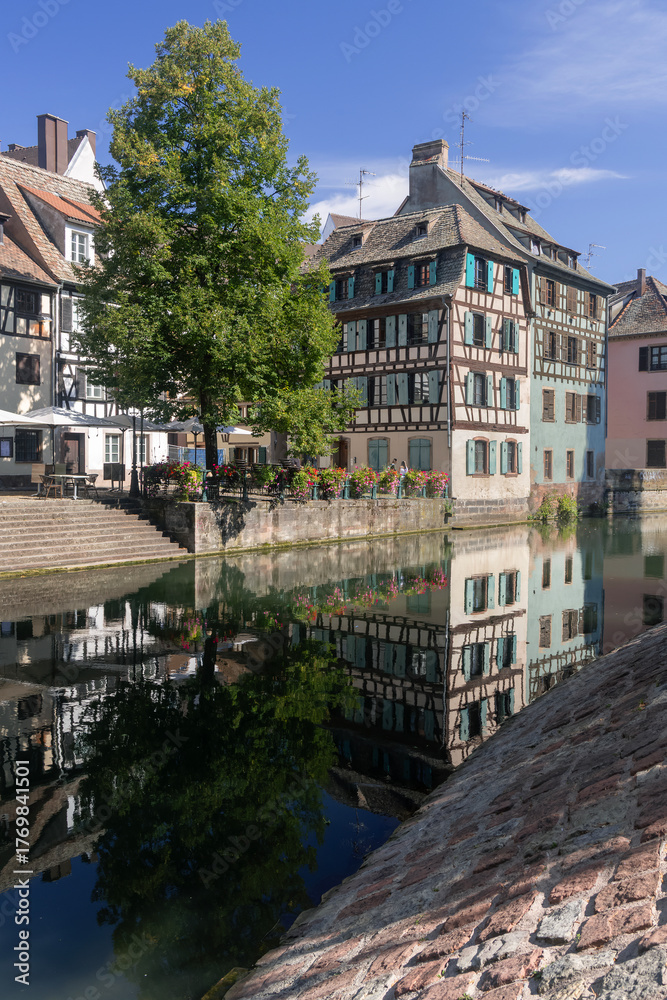 Fototapeta premium Strasbourg, France - August 26th 2025 : View of the Tanner's Quarter with half-timbered buildings and the Ill river and reflections on the water.