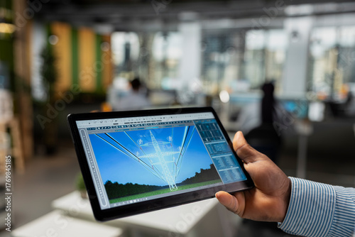 Close up of engineer using tablet to refine transmission tower systems, improving renewable energy integration. RD expert uses touchscreen device in office to design eco power lines infrastructure