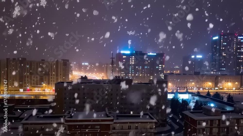 This enchanting video captures a snowy night in the city, where delicate flakes fall gently against a backdrop of illuminated skyscrapers. The warm glow from streetlights reflects off the rooftops, cr