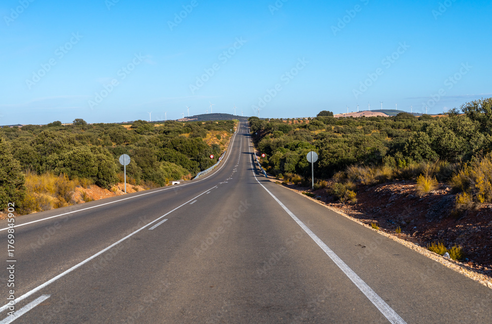 Obraz premium Empty road winds through arid landscape with wind turbines.