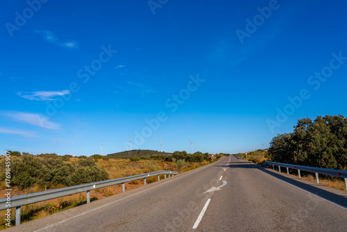 Open road with wind turbines under a clear blue sky.