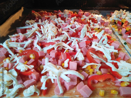 cooking delicious pizza with sausage, tomatoes and cheese at home close-up. ingredients for baking cheese, sausage, tomato sauce and tomatoes, corn, olives. delicious snack for children and adults