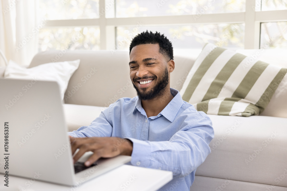 Fototapeta premium Smiling African man typing on laptop keyboard