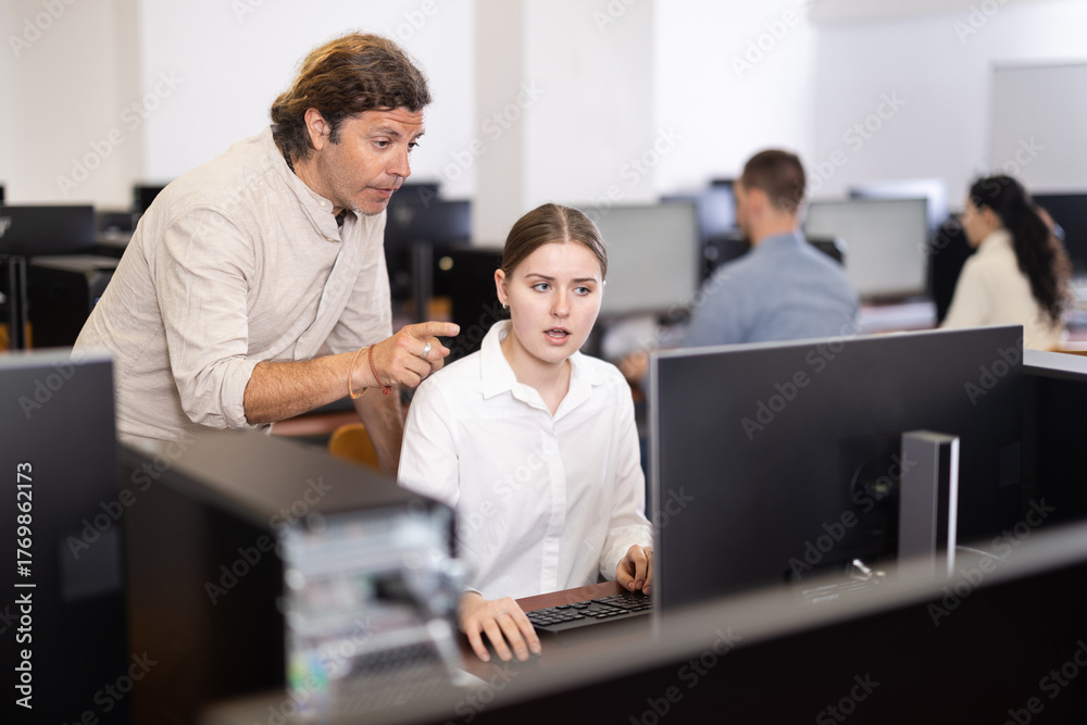 Obraz premium Man teacher helps girl with learning on computer in university computer class