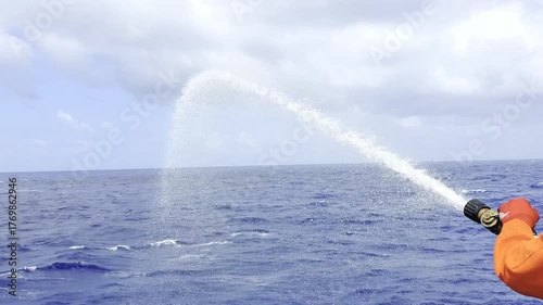 Crew tests fire hose on cargo ship, water flowing overboard during safety equipment drill at sea 1 realistic view of maritime safety procedures and shipboard emergency preparedness.