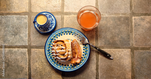 breakfast setting consisting of cinnamon roll, bacon strip, ruby red grapefruit juice and single shot of espresso coffee 