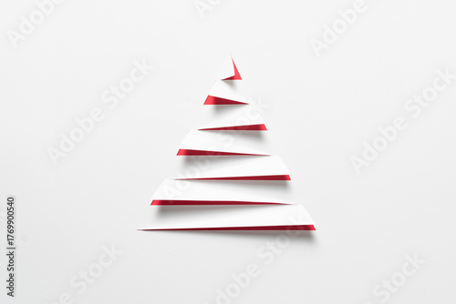 A minimalist white paper cut in a stepped, triangular shape to evoke a Christmas tree, with a striking red background showing through the cuts, for Christmas celebration or simple winter themes.