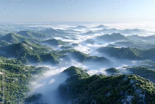 An aerial view showcases mountain ranges enveloped in mist and lush greenery under a clear sky.