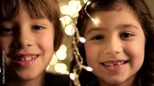 Adorable young brother and sister smiling together, surrounded by warm, glowing fairy lights.