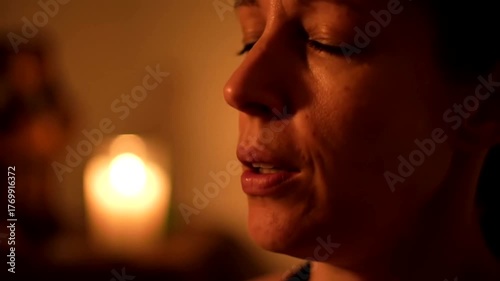 woman with closed eyes meditates peacefully in the warm, soft glow of a single candle.
