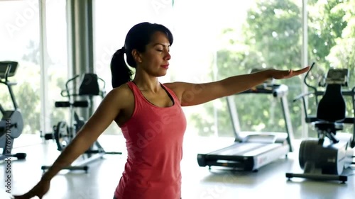 Woman stretching arms in gym with exercise equipment.