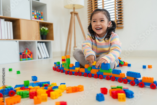 toddler girl playing building blocks or plastic bricks toy at home