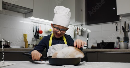 Young boy in a kitchen having fun with a fluffy rabbit in a pan, wearing a chef hat and apron, creating a joyful and playful cooking scene