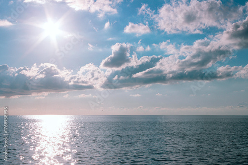 Sea landscape with bright sun reflecting on water surface and clouds in blue sky