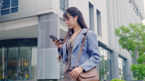 Young business businesswoman walking outdoor, happy professional travel near modern office buildings, using smartphone with earphones, enjoying urban environment and digital connection.