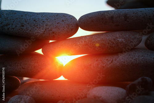 Sunset sun shining through stacked stones on the shore
