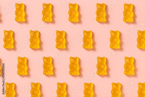 Pattern of yellow gummy bears arranged neatly on a light pink background in a repeating grid format