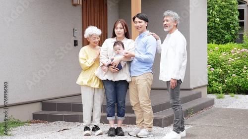 住宅の前で笑顔で赤ちゃんを囲む三世代家族
