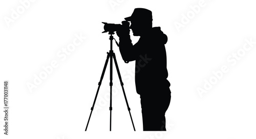 A person wearing a cap and hoodie captures a photograph using a professional camera mounted on a tripod silhouette