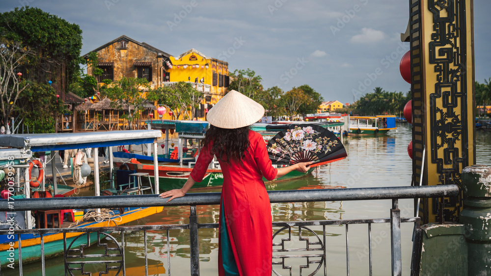 Fototapeta premium A woman in traditional Vietnamese cultural clothing in the ancient city of Hoi An on a bridge
