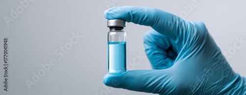 Doctor in blue glove holding a vaccine vial against a neutral background, close-up photo