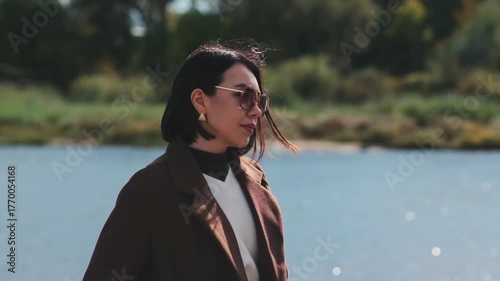 woman enjoying peaceful park walk near the river, casual autumn day with sunglasses and gentle wind movement