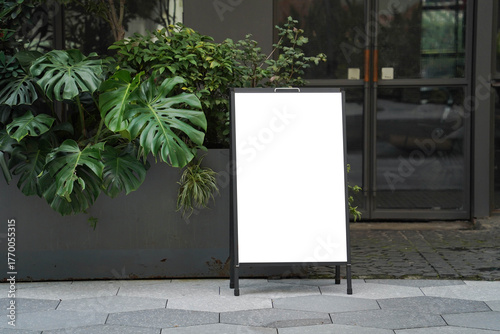 Blank white outdoor advertising stand or sandwich board mock up template. Clear street signage board placed by an outdoor dinning area of a restaurant. Background texture of standee on street.