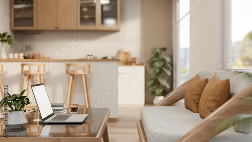 Fototapeta Naklejka Na Ścianę i Meble -  Laptop and books on glass top table aside sofa couch across kitchen counter in apartment living room