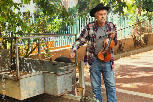 Senior Musician with Violin Beside Rustic Trailer Outdoors