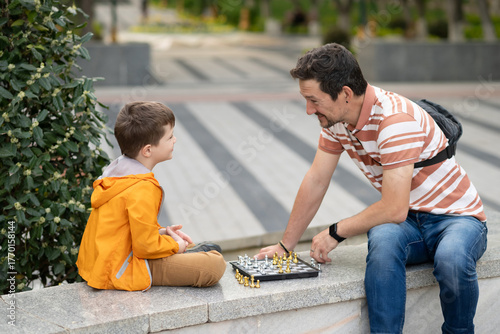 Boy with father playing chess outdoor. Learning strategic game. Education.