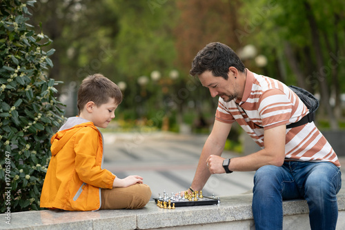 Boy with father playing chess outdoor. Learning strategic game. Education.
