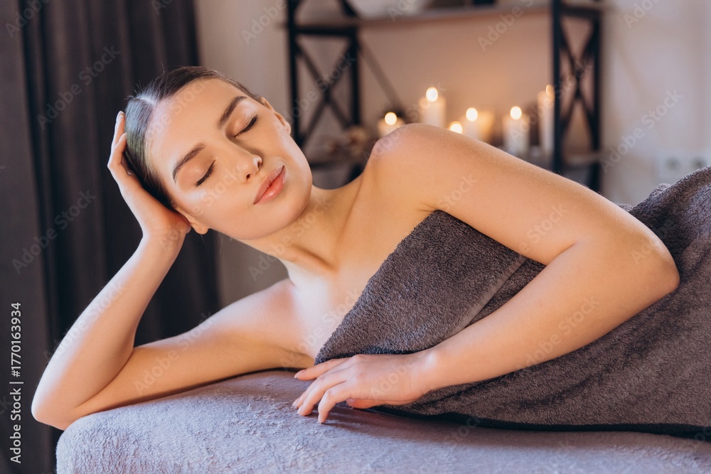 Obraz premium Woman relaxing on massage table with candles in background
